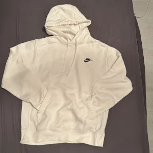 Vit hoodie från Nike - Säljer en stilren vit hoodie från Nike med klassisk logga på bröstet. Hoodien har en bekväm passform med känguruficka och justerbar huva. Perfekt för en avslappnad look.