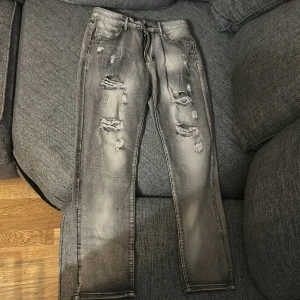 Grå slitna jeans - Snygga grå jeans med slitningar på framsidan för en trendig look. De har en klassisk femficksdesign och en bekväm passform. Perfekta för en avslappnad stil.