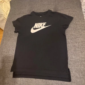 Svart t-shirt från Nike - Säljer en svart t-shirt från Nike med det klassiska logotyptrycket i vitt på framsidan. T-shirten har en normal passform och korta ärmar, perfekt för en sportig look.