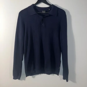 Pikétröja - Snygg mörkblå pikétröja  med långa ärmar och klassisk krage. Perfekt för en stilren look. Tröjan har knappar framtill och är tillverkad i ett mjukt material.