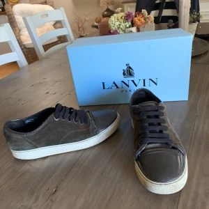 Bruna sneakers från Lanvin - Snygga bruna sneakers från Lanvin i mocka med vita sulor. Skorna har snörning och en stilren design som passar perfekt för en avslappnad look. Lite slitningar på cap toen på höger skor därför så billigt pris