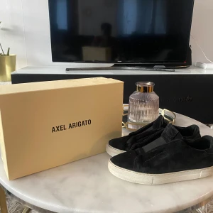 Svarta sneakers från Axel Arigato - Snygga svarta sneakers från Axel Arigato med en stilren design. Skorna har en vit sula och är tillverkade i mocka. Perfekta för en avslappnad och trendig look.