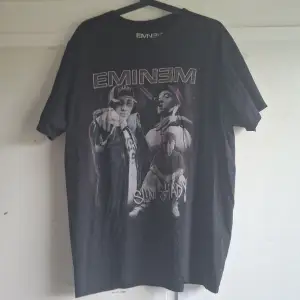 Säljer en svart Eminem t-shirt i storlek XL. T-shirten är gjord av 100% bomull och har ett tryck med Eminem och Slim Shady på framsidan. Perfekt för fans av Eminem! T-shirten är i bra skick och redo att bäras.