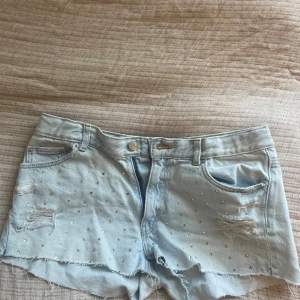 Ljusblå jeansshorts från Gina Tricot - Säljer ett par ljusblå jeansshorts från Gina Tricot Young. De har små diamanter på framsidan. Säljer dessa pga att de är försmå för mig💕💕