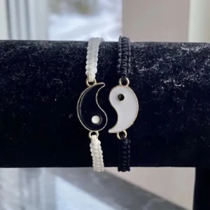 Yin och Yang armband i svart och vitt - Säljer ett par snygga Yin och Yang armband. Det ena armbandet har en vit flätad rem med en svart och vit Yin och Yang-symbol, medan det andra har en svart flätad rem med en vit och svart symbol. Perfekta för att matcha med din outfit och ge en balanserad look!