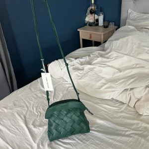 Grön axelväska Carin Wester - Snygg grön axelväska från Carin Wester med ett flätat mönster. Väskan har en justerbar axelrem och en dragkedja upptill. Perfekt för att ge en stilren touch till din outfit. Liknande Bottega. 