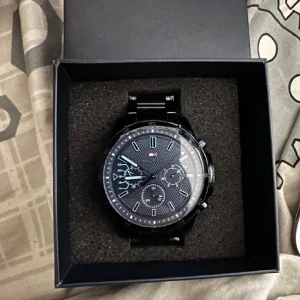 Svart klocka från Tommy Hilfiger - Snygg svart klocka från Tommy Hilfiger med flera urtavlor och en stilren design. Klockan har en svart länkarmband och tydliga markeringar på urtavlan. Perfekt för den som vill ha en elegant och funktionell accessoar. Tyvärr funkar den dessvärre inte vet inte varför förmodligen pga batteriet. därav det billiga priset. Ny pris 2800kr.