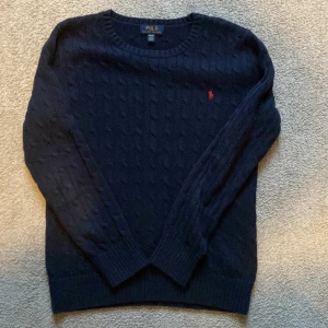 Mörkblå kabelstickad tröja från Ralph Lauren - Säljer en snygg mörkblå stickad tröja från Ralph Lauren med kabelstickat mönster och det klassiska röda logotypbroderiet på bröstet. Perfekt för kyliga dagar!                XL i barnstorlek=M😊 hör av er vid frågor eller prisförslag!