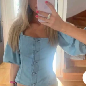 Blå jeansblus med knappar - Snygg blå jeansblus med knappar framtill och puffiga trekvartsärmar. Perfekt för en avslappnad stil med en touch av elegans.