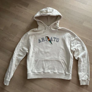 Hoodie från Axel Arigato - Säljer en stilren beige hoodie från Axel Arigato med en färgglad fågelbroderi och text på bröstet. Storlek S. Använd endast ett fåtal gånger. Djur/rökfritt hem