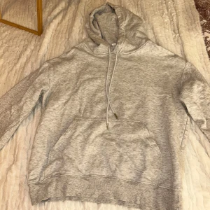 Grå hoodie från H&M - Säljer en stilren grå hoodie från H&M i storlek XS. Den har en klassisk design med en stor ficka framtill och justerbar huva med dragsko. Perfekt för en avslappnad look.
