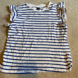 Randig topp med volangärmar - Säljer en söt randig topp med blå och vita ränder. Toppen har volangdetaljer vid ärmarna och en rund halsringning. Perfekt för en gullig sommar stil💞