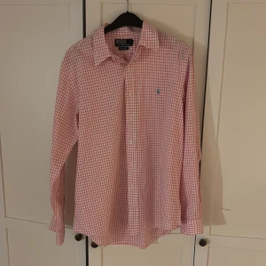 Rutig skjorta från Polo Ralph Lauren - Säljer en stilren rutig skjorta från Polo Ralph Lauren i rosa och vit. Skjortan har långa ärmar och knappar framtill. Perfekt för en klassisk look med en touch av färg.