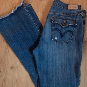 Blå jeans med lock på fickorna - Säljer ett par klassiska blå jeans från Levis modell 515 med en snygga fickor (ficklock). Det står ingen storlek men jag skulle gissa på att de är 29/30 i midjan. Jeansen är andvända men hyfsat bra skick. De är slitna nertill och har gått sönder lite längst ner på vänstra benet. 