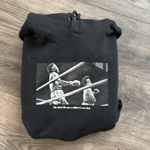 Svart Rocky Balboa hoodie från Pull&Bear - Säljer en svart hoodie från Pull&Bear med Rocky Balboa-tema. Framsidan har ett tryck av en boxningsscen och texten 'His whole life was a million-to-one shot'. Baksidan har texten 'ROCKY BALBOA THE ITALIAN STALLION'. Perfekt för filmälskare och boxningsfans!