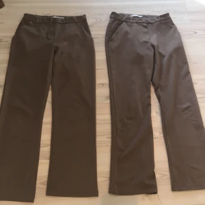 2 par Bruna kostymbyxor - Säljer två par bruna kostymbyxor med rak passform. Byxorna har hällor för bälte och stängs med knapp och dragkedja. De är samma färg även fast det inte ser Urban på bilden. Båda är samma storlek. Ett par för 50 och båda för 80 kr. På sista bilden visas ett par av byxorna som har några fläckar.  Även om de är väldigt små.
