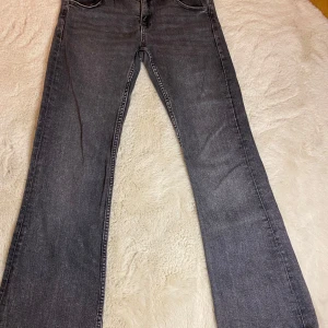Grå jeans från Gina Tricot - Snygga grå jeans från Gina Tricot i en klassisk bootcut-stil. De har en bekväm passform med fickor och knappdetaljer på bakfickorna. Perfekta för en avslappnad look. OBS de är uppsydda några centimeter! Lite mer åt 158 hållet 