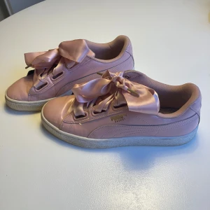 Rosa sneakers från Puma - Snygga rosa sneakers från Puma med breda sidenband som snörning. Skorna har en glansig yta och en vit sula. Perfekta för en trendig look med en touch av elegans.
