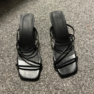 Svarta sandaler med klack - Snygga svarta sandaler med smala remmar och fyrkantig tå. De har en elegant klack och är perfekta för en stilren look. Storlek dam 37.