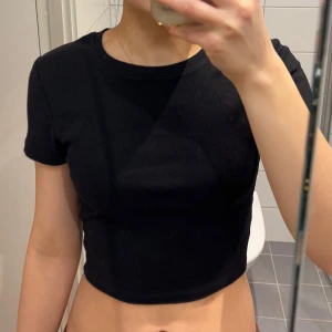 Svart croppad t-shirt - Säljer en stilren svart croppad t-shirt med korta ärmar. Perfekt för en avslappnad look. Passar bra till jeans eller kjol.