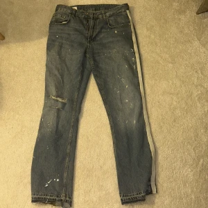 Blå jeans med slitningar - Säljer ett par blå jeans med slitningar och färgstänk för en cool, avslappnad look. Byxorna har en rak passform och klassisk femficksdesign. Perfekta för en casual stil. Byxorna är helt slutsålda. Nypris 699.