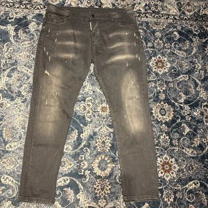 Grå jeans från Dsquared2 - Snygga grå jeans från Dsquared2 med en cool, sliten look och färgstänk. De har en klassisk femficksdesign och knappgylf. Perfekta för en trendig och avslappnad stil.    Sitter inte lika tight som de flesta gör 