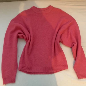 Rosa stickad tröja  - Säljer en mysig rosa stickad tröja från Nelly. Tröjan har långa ärmar och ribbade kanter vid ärmslut och nederkant. Perfekt för kyliga dagar!