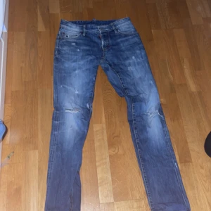 Blå jeans från Dsquared2 - Snygga blå jeans från Dsquared2 med slitna detaljer och en klassisk femficksdesign. Jeansen har en knappgylf och är tillverkade i Italien. Perfekta för en avslappnad stil. De är äldre modell men dessa är äkta storlek 46