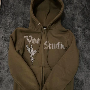  hoodie från Vonstudio - Säljer en olivgrön hoodie från Vonstudio med dragkedja och en snygg fågel- och textdesign i glittriga detaljer på framsidan. Denna tröjan finns ej att köpa längre o är dessutom limited edition. Perfekt för en avslappnad stil med en touch av bling. 🕊️✨