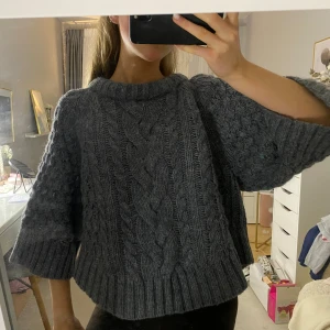 Grå stickad tröja med flätmönster - Säljer en mysig grå stickad trekvartsärmad tröja med ett flätmönster framtill. Storlek S