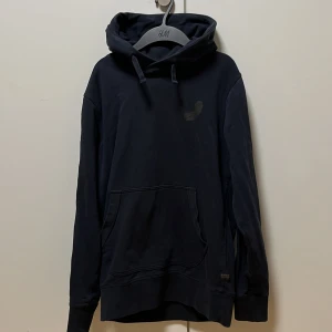 Svart hoodie från g-star  - Säljer en stilren svart hoodie från G-star. Den har en klassisk design med en stor ficka framtill och justerbar huva. Perfekt för en avslappnad look.Storlek S, skick 8/10 Inga hål eller liknande. Sitter lite mer åt slim fit hållet. 