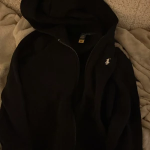 Svart hoodie från Ralph Lauren - Säljer en stilren svart hoodie från Ralph Lauren med dragkedja och den klassiska loggan på bröstet. Perfekt för en avslappnad look! ( det är M i barnstorlek så för 8-10 år) Testad en gång, inget mer! Nypris 1000 kr. Pris kan diskuteras!