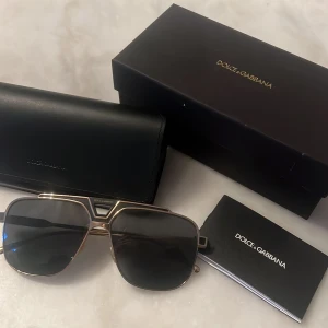 Solglasögon från Dolce & Gabbana - Snygga solglasögon från Dolce & Gabbana med en elegant guldfärgad ram och mörka linser. Perfekt för att ge en lyxig touch till din stil. Kommer med originalfodral och förpackning. Säljer pga att jag inte behöver de längre, de är köpta i synsam men har tappat bort kvittot. Kan mötas upp i Stockholm. Köpta för 1700