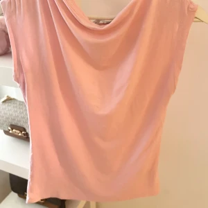 Rosa ärmlös topp - Säljer en söt rosa ärmlös topp med draperad hals. Perfekt för varma sommardagar eller som ett lager under en jacka. Toppen har en mjuk och bekväm passform.