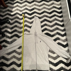 Grå hoodie tracksuit från Polo Ralph Lauren - Säljer en stilren grå hoodie från Polo Ralph Lauren. Den har en dragkedja framtill och en klassisk logga på bröstet. Perfekt för en avslappnad look. Har kvittobevis 