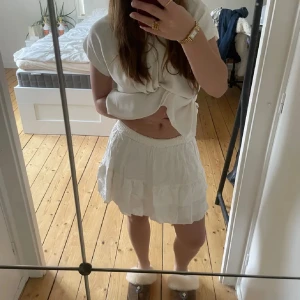 Vit kortkjol med volang - Säljer en söt vit kortkjol med volangdetaljer. Perfekt för varma sommardagar. Kjolen har en elastisk midja för en bekväm passform.