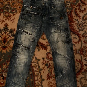 Blå jeans med detaljer från Kosmo Lupo - Coola detaljrika baggy jeans från Kosmo Lupo med nitar och andra coola detaljer, midjemått är 85cm och inre ben längd 82cm 