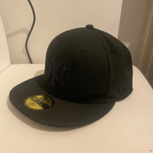 Svart keps med NY-logga 58,7cm - Snygg svart keps med broderad NY-logga framtill. Perfekt för en casual look eller sportiga aktiviteter. Kepsen har en platt skärm och är i en klassisk stil.(PRISET KAN DISKUTERAS)