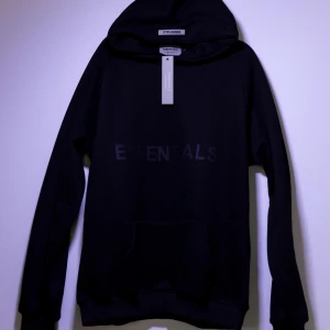 Essentials Hoodie - Helt ny Essentials hoodie. Tröjan har en klassisk design med en känguruficka framtill och en justerbar huva. Perfekt för en avslappnad look.