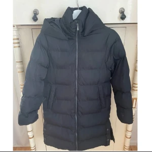 Svart dunjacka från McKinley - Säljer en svart dunjacka från McKinley med dragkedja och huva. Jackan är långärmad och perfekt för kalla dagar. Den är använd 1-2 gånger.