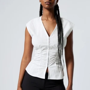 Vit randig blus från Weekday - Snygg vit blus med tunna blåa ränder från Weekday. Blusen har en v-ringad design och är ärmlös. Aldrig använd endast provad!