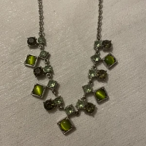 Halsband med gröna stenar  - Unikt halsband med en kedja i silverfärg och dekorativa gröna stenar i olika former. 