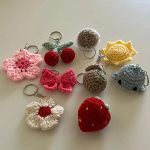 Handgjorda virkade nyckelringar - Unika handgjorda virkade nyckelringar i olika former och färger. Inkluderar en röd jordgubbe, en vit blomma med röd mitt och en blå val. Perfekta som personliga accessoarer eller presenter.