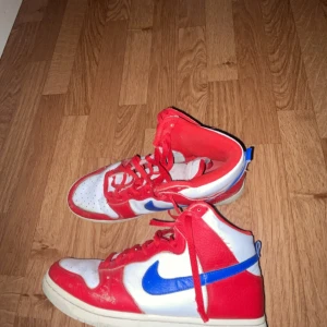 Nike sneakers i rött, vitt och blått - Snygga Nike sneakers i en fräsch kombination av rött, vitt och blått. Skorna har klassisk snörning och en sportig design som passar perfekt för en aktiv livsstil.