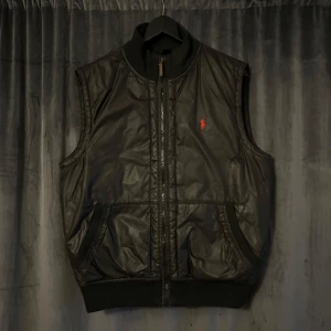 Svart dunväst från Polo Ralph Lauren - Snygg svart dunväst från Polo Ralph Lauren med röd broderad logotyp på bröstet. Västen är vintage men har inga större användnings skador. Kontakta gärna vid frågor 🙂