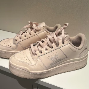 Beige sneakers från Adidas - Snygga beige sneakers från Adidas med klassisk design och snörning. Skorna har en diskret logga på sidan och perforerade detaljer på ovansidan för extra stil. Perfekta för en avslappnad look.