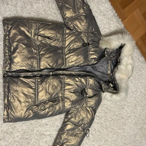 Silverfärgad pufferjacka med pälsdetaljer - Skit snygg och mysig silverfärgad pufferjacka med vit fluffig päls på huvan. Perfekt nu för vintern för att se bra ut & hålla sig extra varm❤️‍🔥Den är oversized och har därför storleken XL men passar alla storlekar då den inte är så jätte lång!  HELT NY JACKA som aldrig är använd🙌🏼 köp nu :)
