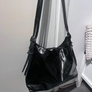 Svart väska från Zara - Snygg svart axelväska från Zara i skinnimitation med stilrena detaljer. Är precis som ny, använd max 2 gånger. Väskan har justerbara band och innerficka med dragkedja. Perfekt som skolväska! Kan mötas i Stockholm eller frakta