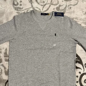 Polo Ralph Lauren Tröja - Snygg grå tröja från Polo Ralph Lauren med klassisk design och broderad logga på bröstet. Perfekt för en stilren och avslappnad look. Helt ny och aldrig använd, alltså helt felfri!