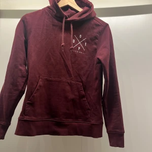 Vinröd hoodie från Dope - Snygg vinröd hoodie från Dope med tryck både fram och bak. Den har en stor ficka framtill och justerbar huva med dragsko. Perfekt för en avslappnad stil. Står S på men är mer en xs om man vill att den sitter pösigt😇